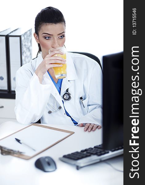 Doctor drinking a glass of juice at her workplace over white background