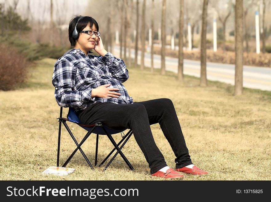 Pregnant woman sitting on lawn listens music under warm sunshine in early spring. Pregnant woman sitting on lawn listens music under warm sunshine in early spring.