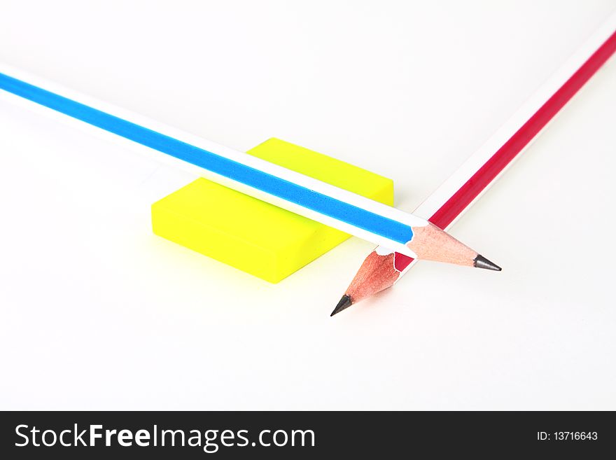 Two colorful pencils and yellow rubber on white crossed