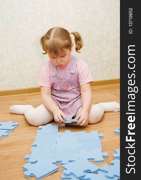 Little girl collects puzzles in a room