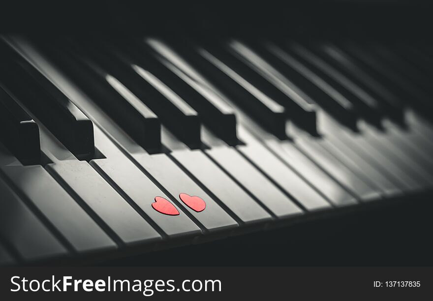 Two small red hearts on the white black keyboard of classic piano close up. Concept of love and romantic music. Copy space. Two small red hearts on the white black keyboard of classic piano close up. Concept of love and romantic music. Copy space