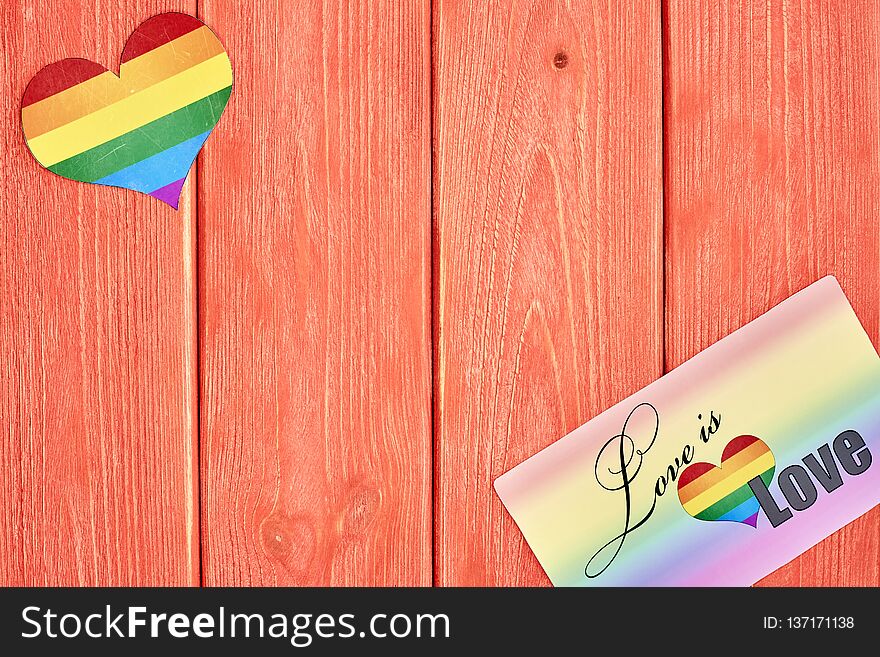 Postcard love is love and a heart with a rainbow of LGBT, on wooden texture background color living coral