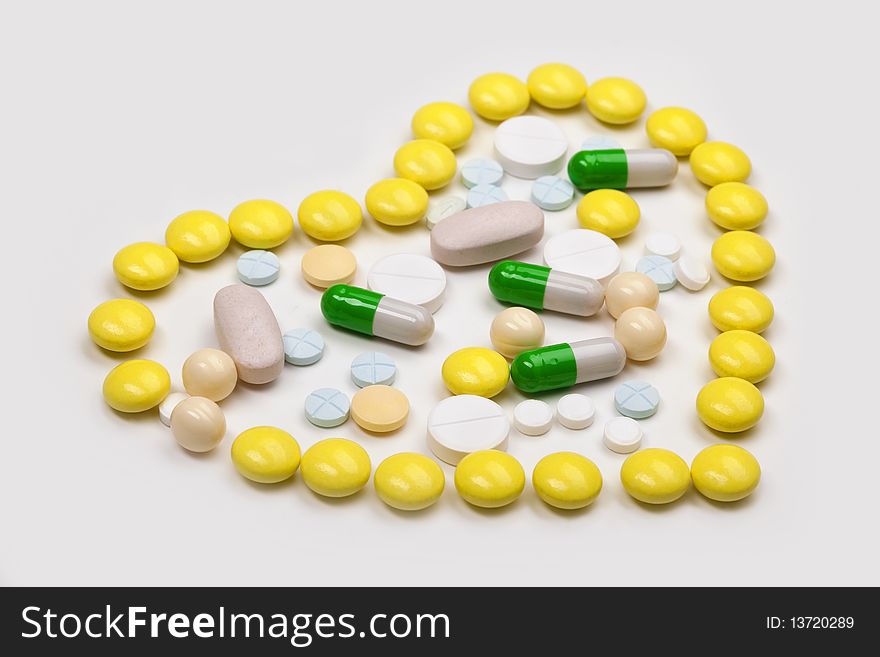 Various colour tablets and capsuls in the shape of a heart on white background