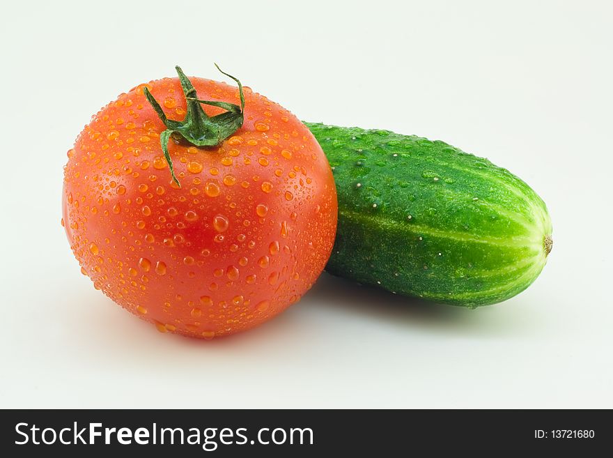 Fresh vegetables: a cucumber and a tomato with water drops on a white background. Fresh vegetables: a cucumber and a tomato with water drops on a white background