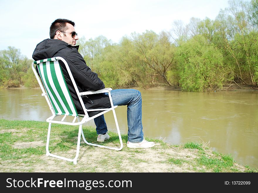 Man is sitting in the chair at the camp in mountains near the river. Man is sitting in the chair at the camp in mountains near the river