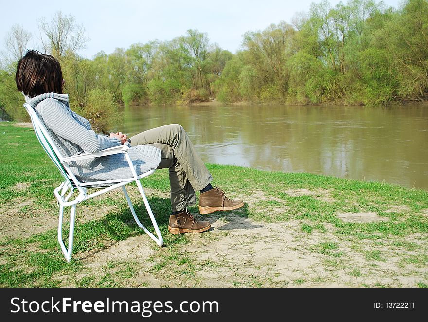 Woman is sitting in the chair at the camp in mountains near the river. Woman is sitting in the chair at the camp in mountains near the river