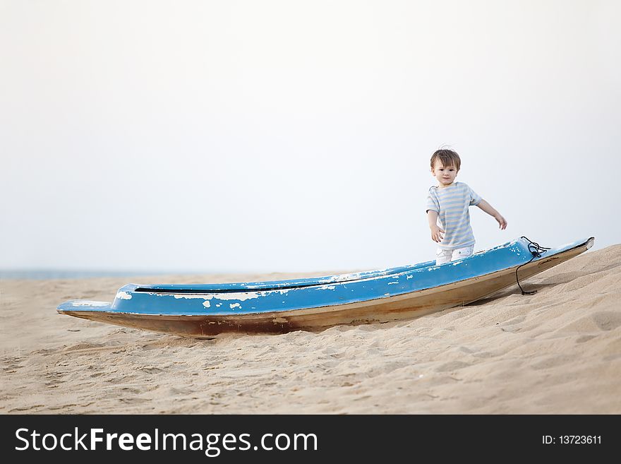 Little boy standing in the boat lying on the beach. Little boy standing in the boat lying on the beach