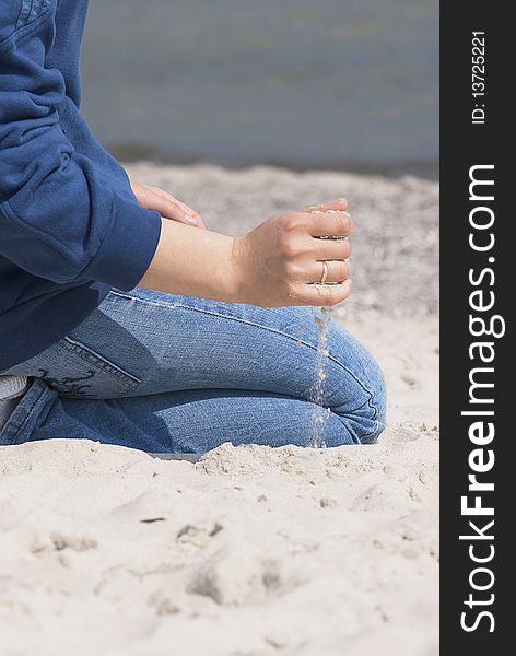 Woman in blue jeans sitting on the beach with the sand pouring out from her hand with the golden ring. Woman in blue jeans sitting on the beach with the sand pouring out from her hand with the golden ring