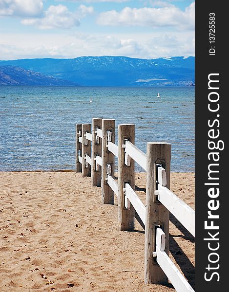 Wooden fence on sandy beach with water and mountains in background. Wooden fence on sandy beach with water and mountains in background