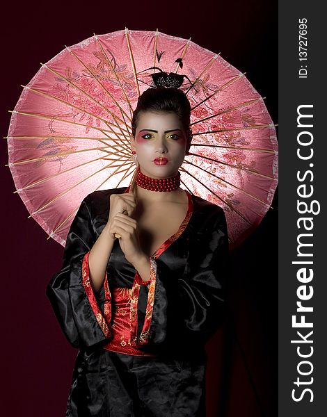 woman wearing geisha costume, holding an umbrella and looking at the camera. Studio shot. woman wearing geisha costume, holding an umbrella and looking at the camera. Studio shot