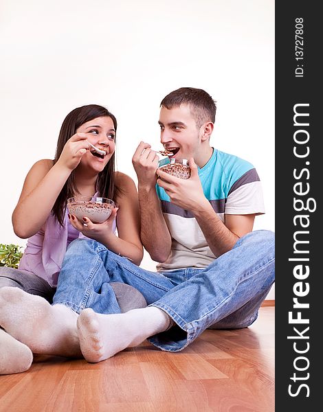 Happy smiling young couple sitting on the floor and eating. Happy smiling young couple sitting on the floor and eating