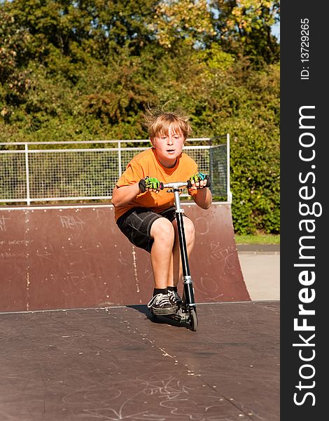 Child, boy is jumping with a scooter over a fun box in the skate parc and enjoying it. Child, boy is jumping with a scooter over a fun box in the skate parc and enjoying it