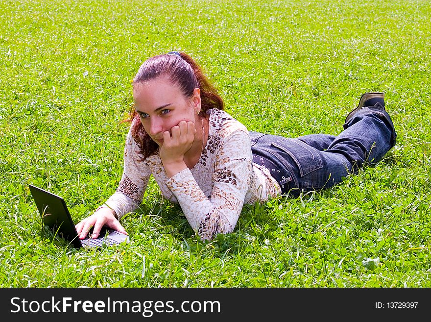 Young girl lying on green grass with laptop. Young girl lying on green grass with laptop