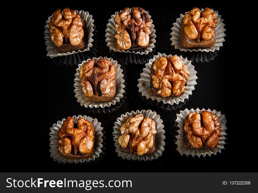 Top view on big group of dark useful handmade candies decorated with walnut on black mirror background. Top view on big group of dark useful handmade candies decorated with walnut on black mirror background