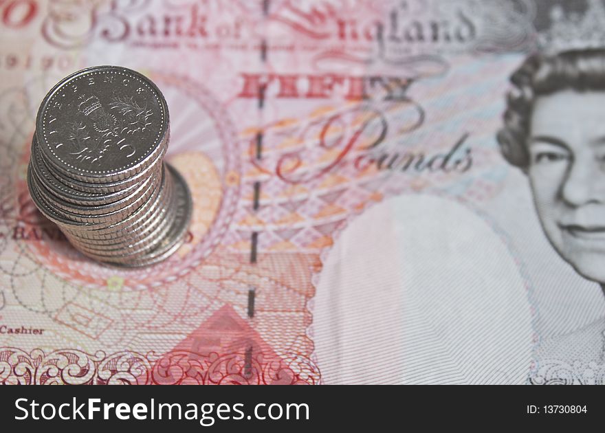 Some five pence pieces stacked on top of a fifty pound note in soft focus. Some five pence pieces stacked on top of a fifty pound note in soft focus