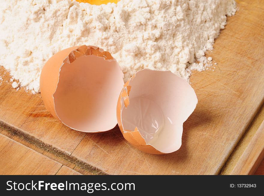 Empty egg next to white flour on cutting board. Empty egg next to white flour on cutting board.