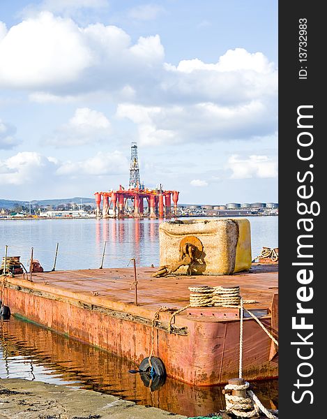 An image of a floating platform with an anchor weight on it and in the distance Invergordon with a large oil rig anchored in the port. An image of a floating platform with an anchor weight on it and in the distance Invergordon with a large oil rig anchored in the port.