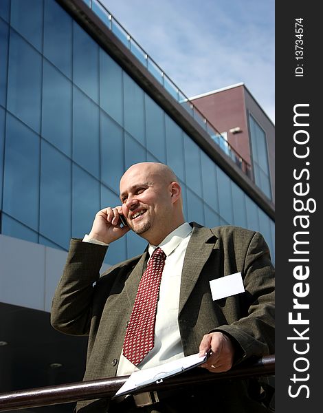 A smiling businessman talking on the phone in front of an office building. A smiling businessman talking on the phone in front of an office building