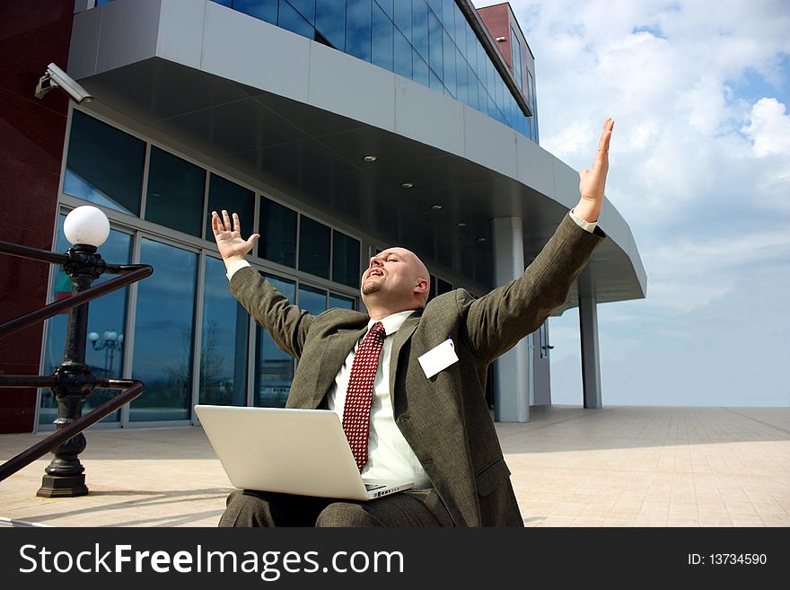 A successful businessman with a laptop in front of a modern office building