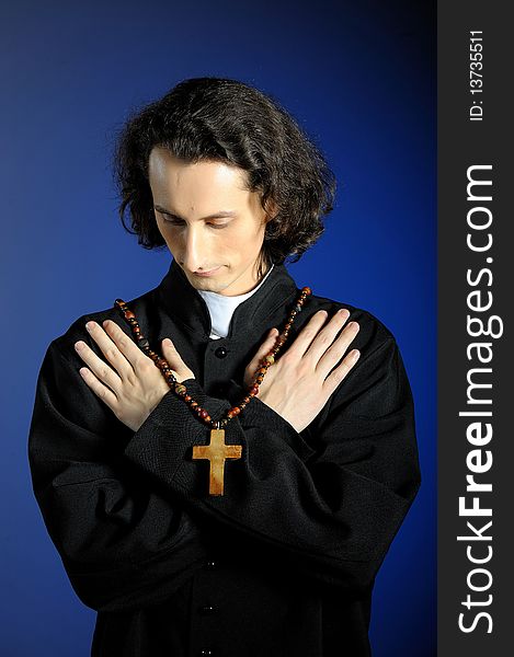 Conceptual portrait of Praying priest with wooden cross. blue background