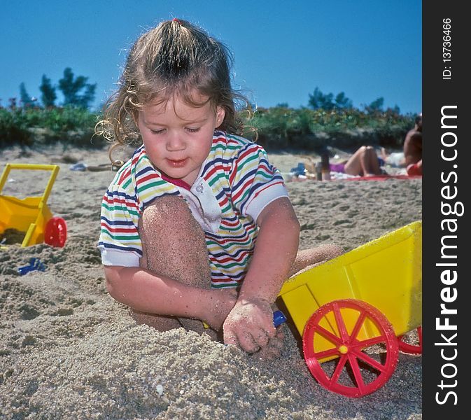 Little girl playing in sand on beach surrounded by beach toys. Little girl playing in sand on beach surrounded by beach toys