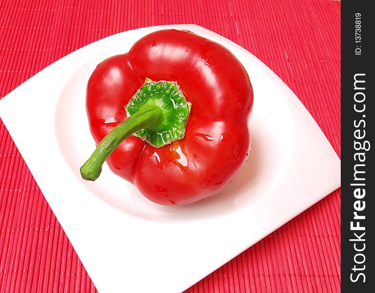 Red,wet,fresh pepper isolated on white plate on red background. Red,wet,fresh pepper isolated on white plate on red background