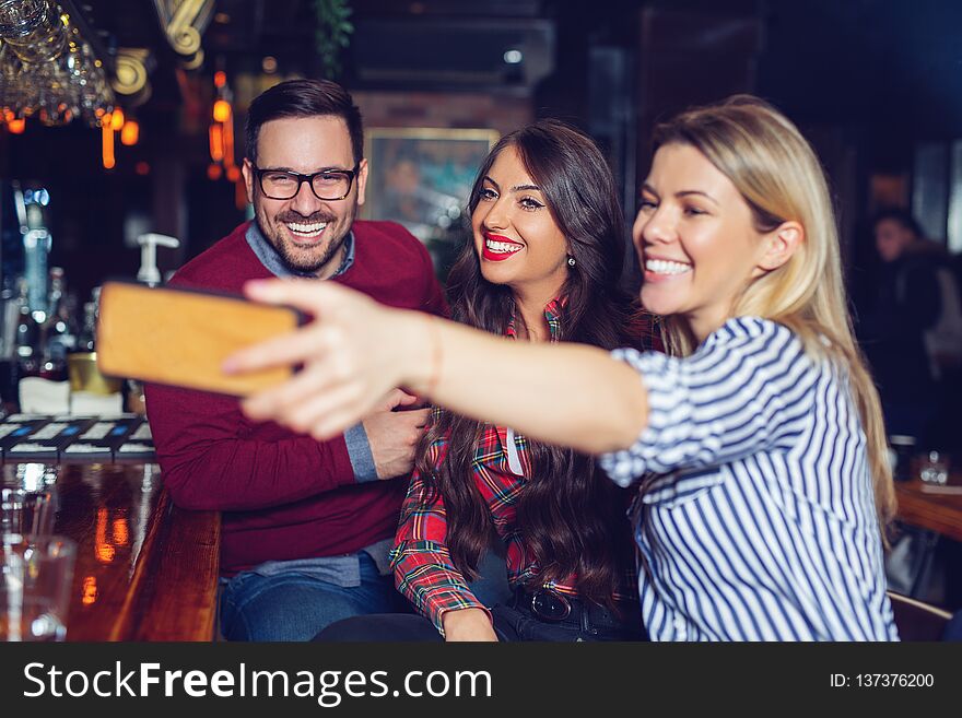 Young beautiful three friends taking selfie in a bar. - Image