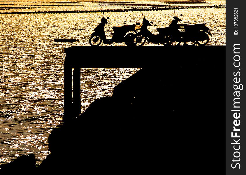 Silhouette of motorcycles on dock with effect of sunset light on sea surface