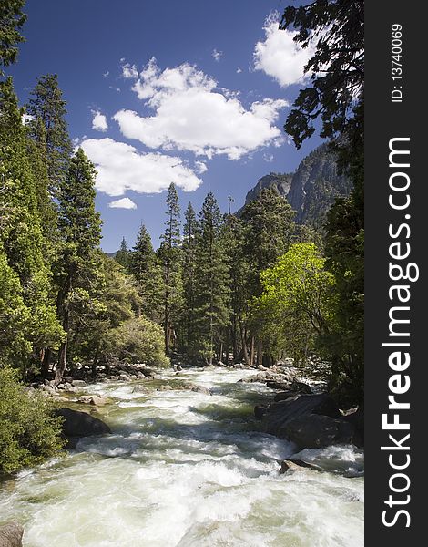 The Merced River flowing through Yosemite Valley with blue sky