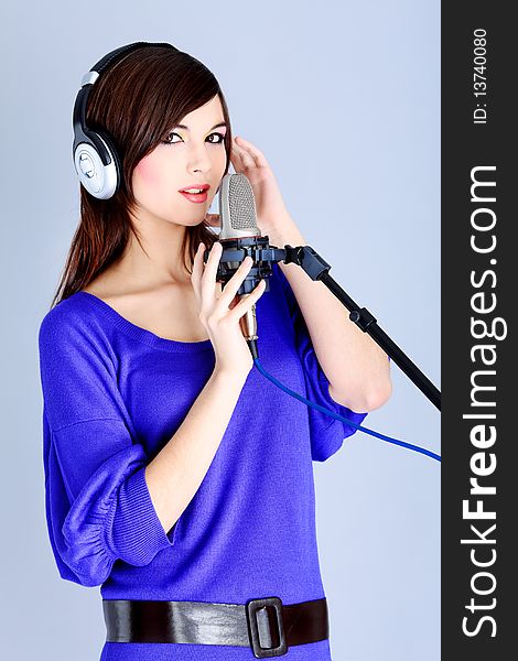 Shot of a pretty young woman in headphones singing a song with a microphone. Shot in a studio.