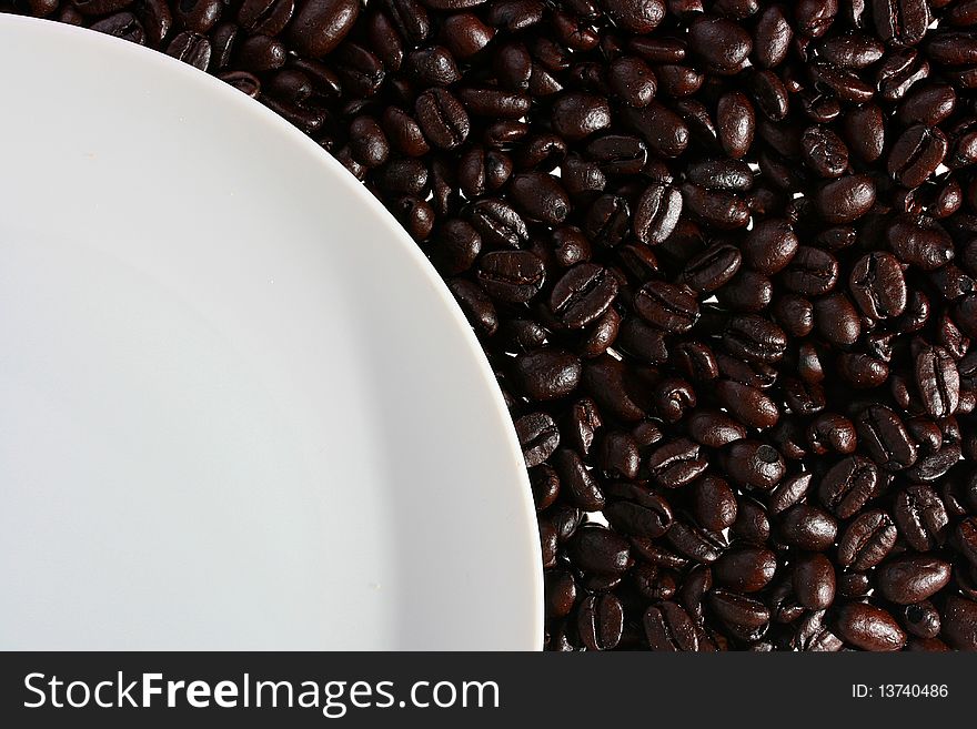 Coffee grains on a back background, from above there is a white plate.