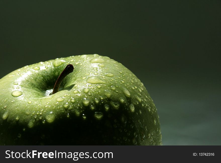 Big green apple with water drops on the dark background