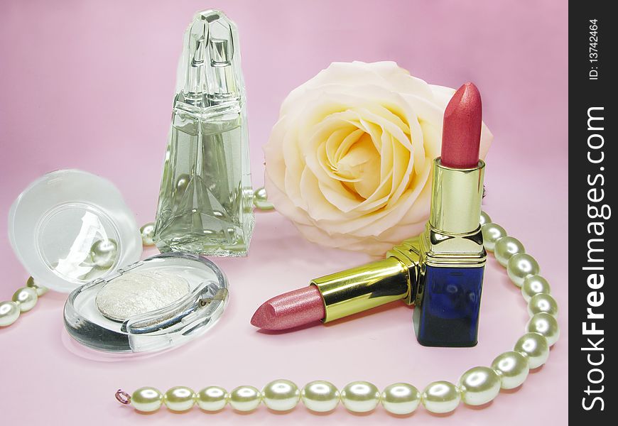 Red lipsticks yellow rose white eye-shadow and perfume on pink background. Red lipsticks yellow rose white eye-shadow and perfume on pink background