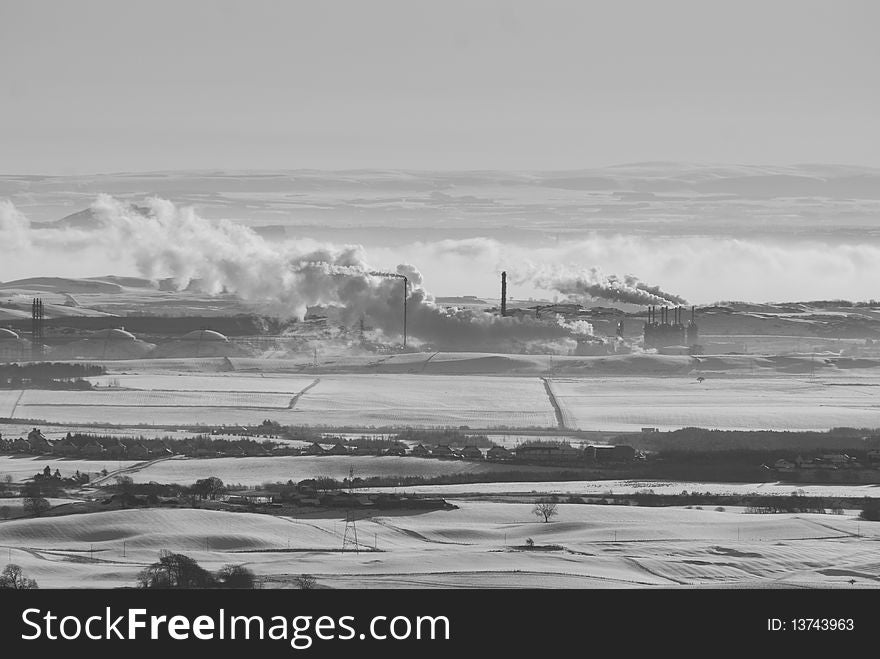 The view from Benarty hill depicts a nearby petro-chemical plant surrounded by snow covered fields with low lying fog in the background. The view from Benarty hill depicts a nearby petro-chemical plant surrounded by snow covered fields with low lying fog in the background