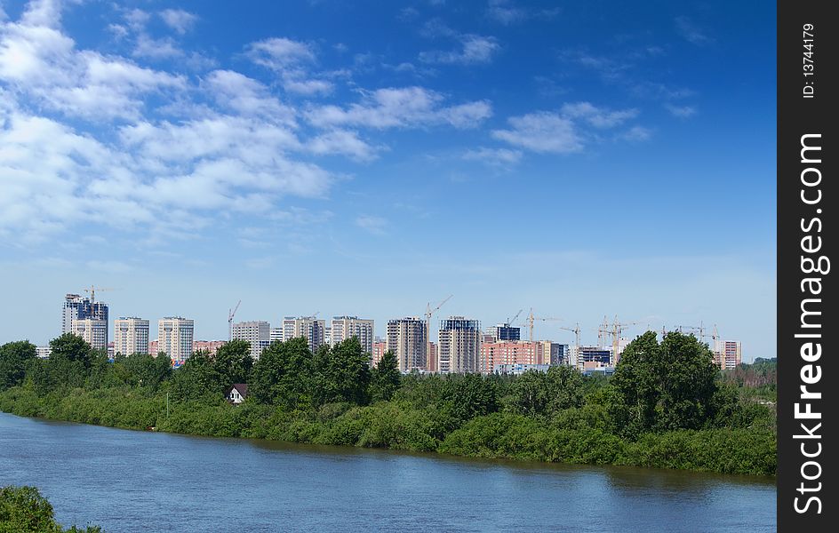 View of a some new residential buildings on a background of cloudy blue sky and river with green coast