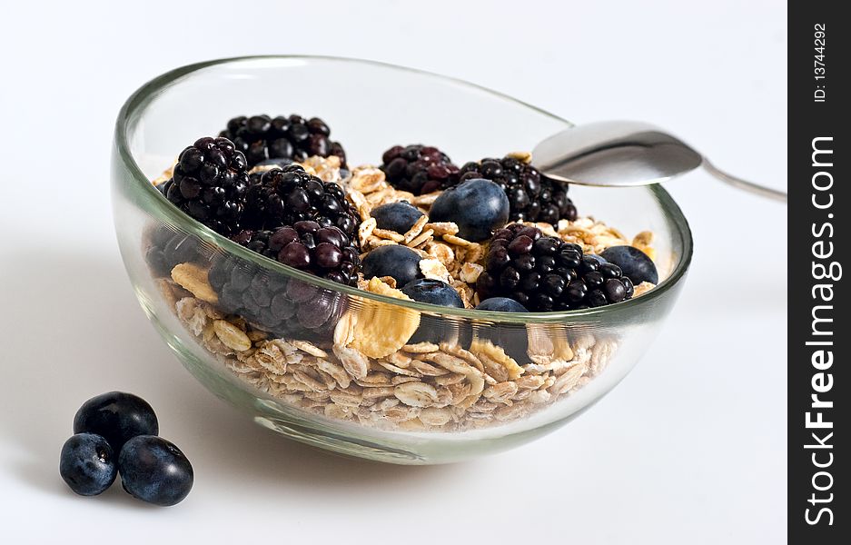 A glass bowl full of muesli, corn flakes, blackberries and blueberries. Selective focus. White background. A glass bowl full of muesli, corn flakes, blackberries and blueberries. Selective focus. White background.