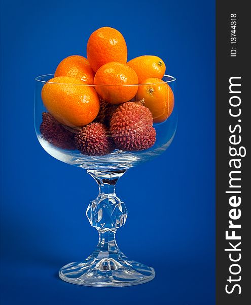 Kumquat and Litchi fruits in a crystal glass on a deep blue background