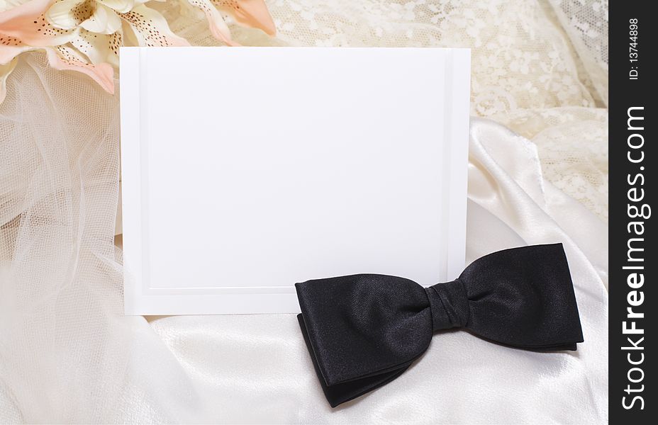 Blank off white border card on ivory satin and lace with black bow tie. Blank off white border card on ivory satin and lace with black bow tie