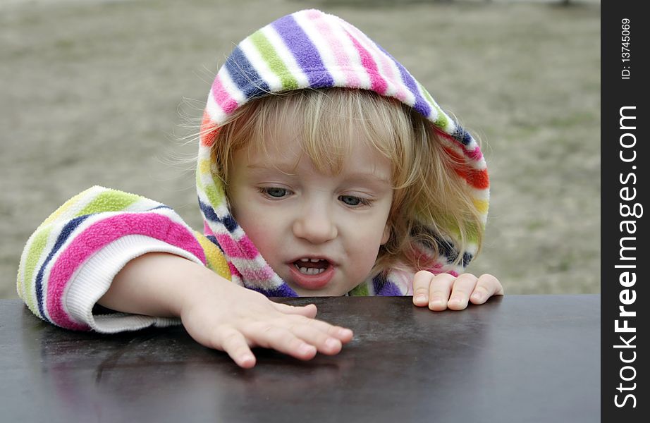 The little girl is exploring the surface of a wooden table. The little girl is exploring the surface of a wooden table