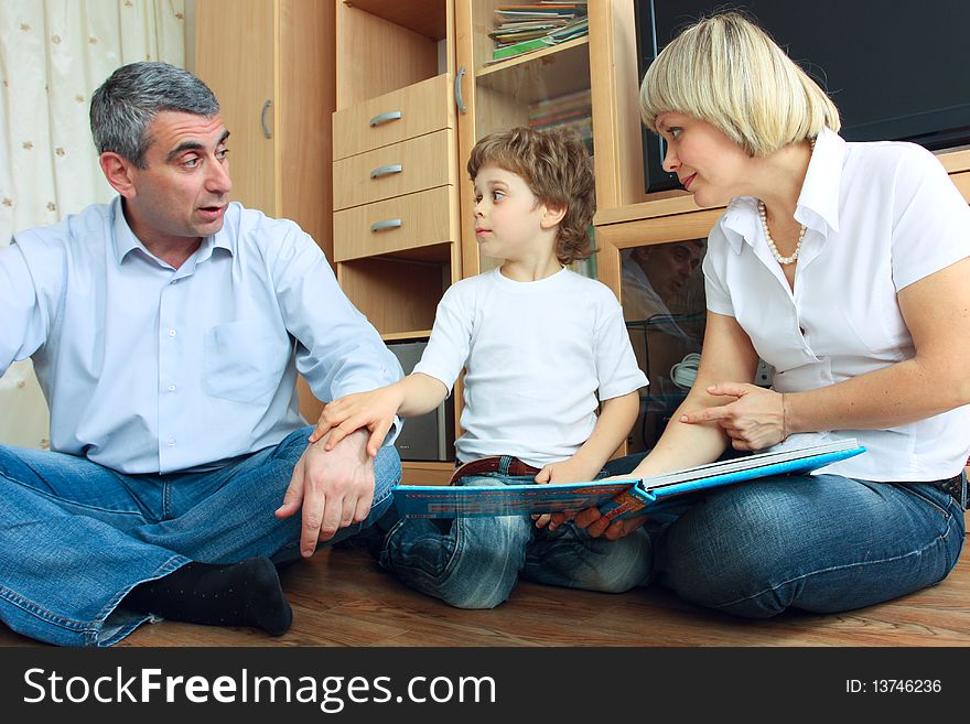 Man, woman and little boy sitting on the floor in living room and reading book. Man, woman and little boy sitting on the floor in living room and reading book