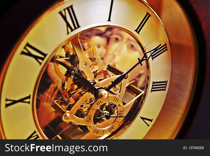 Open-gearing transparent clock with the Virgin Mary icon appearing through glass, blur background. Open-gearing transparent clock with the Virgin Mary icon appearing through glass, blur background
