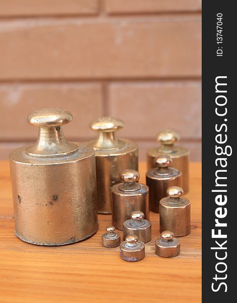 Antique weights from an old scale, made of brass, on a wooden surface and with a brick background. Antique weights from an old scale, made of brass, on a wooden surface and with a brick background