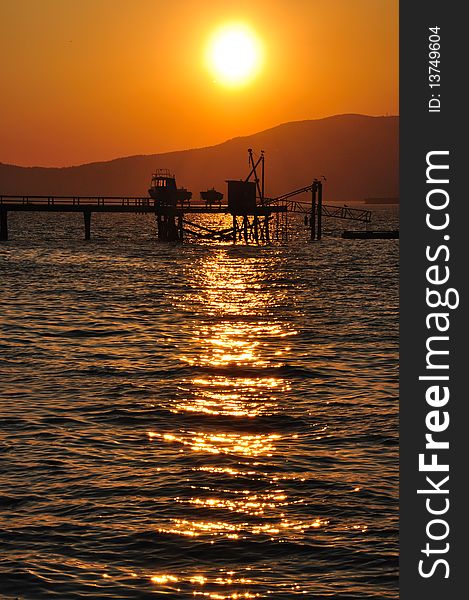 Warm sunset over the sea with silhouetted dock and mountain. Warm sunset over the sea with silhouetted dock and mountain.