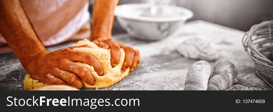 Mid section of baker kneading dough in bakery shop