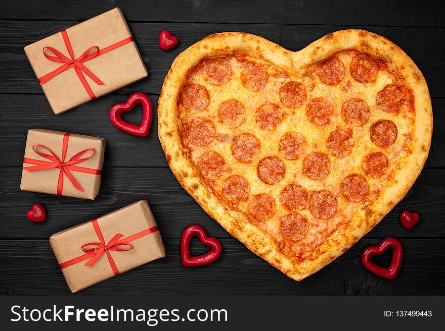 Pizza shaped heart with gift box for Valentine`s Day romantic concept on rustic dark black background. Top View. Flat lay.