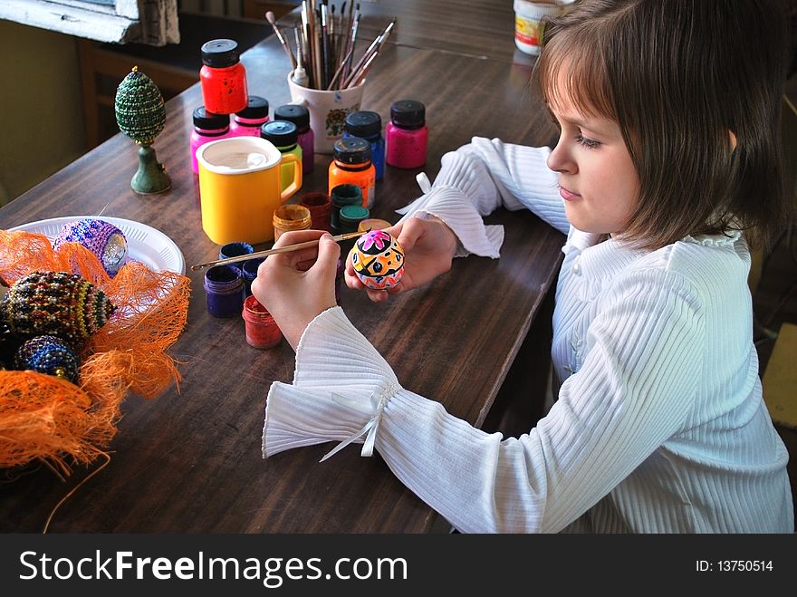 Schoolgirl is paint of easter egg by paintbrush