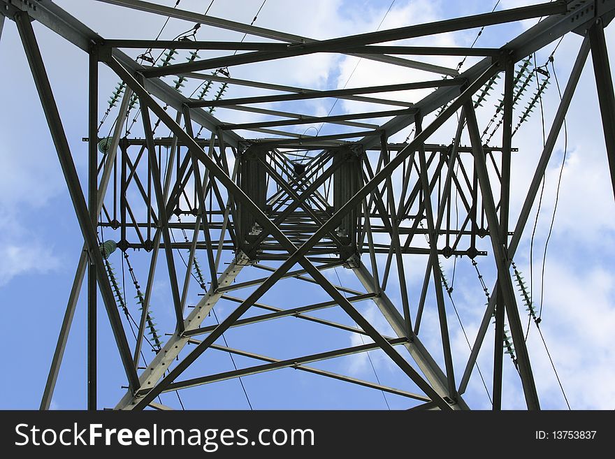 Support metal high-voltage with isolators and wires on a background of the blue sky with clouds.