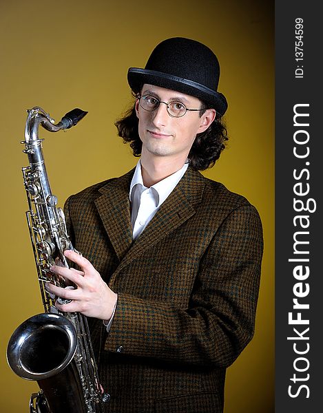 Portrait of young english gentleman in bowler hat holding saxophone. yellow background