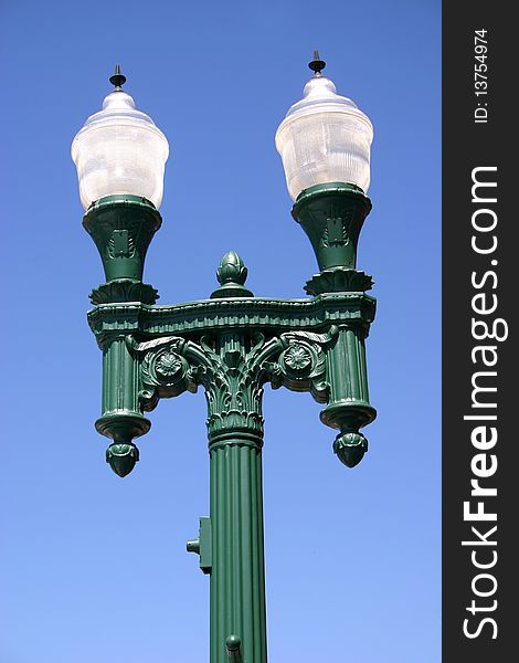 Twin lamps sit atop a green post, against a blue sky