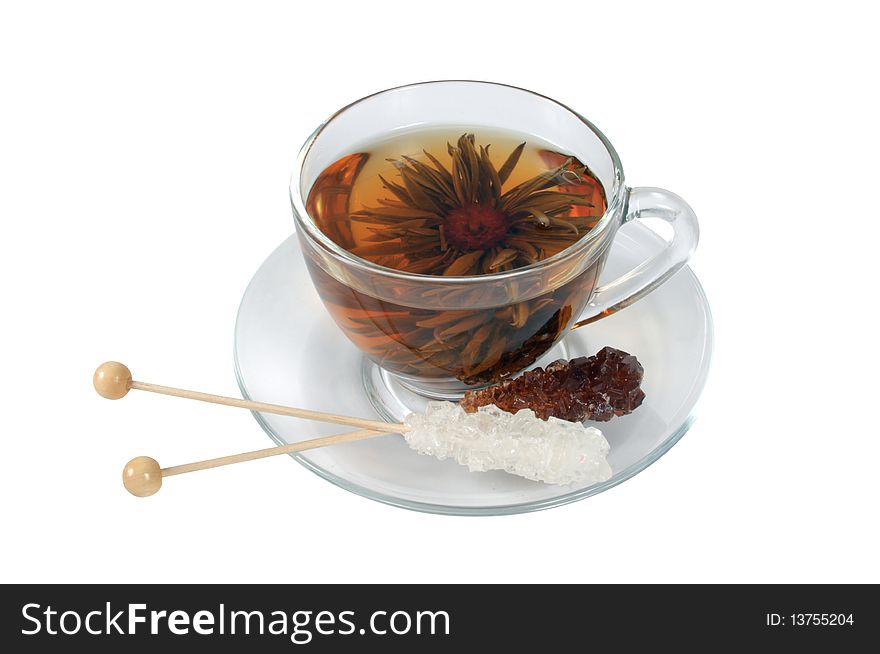 Transparent cup of Chinese tea in the form of decorative flower and two sticks with decorative - white and brown sugar on white background.